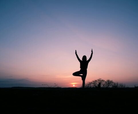 person balanced in tree pose in silhouette against a sunset at Ostara